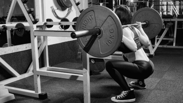 A woman is performing a squat exercise with a heavy barbell in a gym setting showcasing strength for Crossfit, 2K Desktop Wallpaper