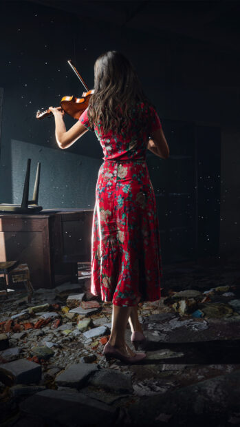 A woman in a floral red dress is playing a violin inside an old room with scattered debris on the floor, 4K Phone Wallpaper