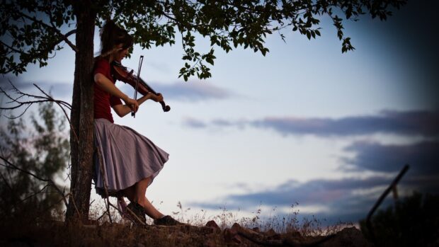 A woman playing violin against a colorful sky while sitting by a tree, 2K Desktop Wallpaper