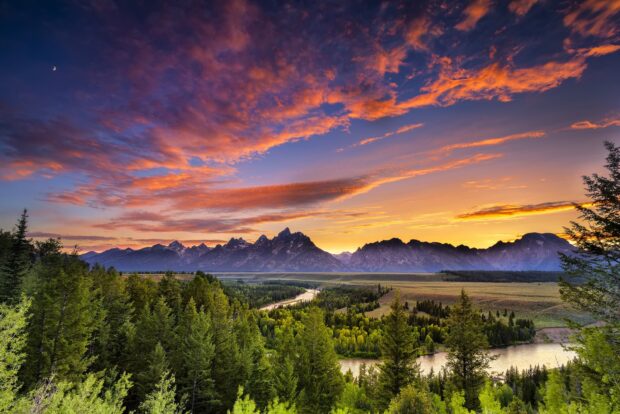 A scenic view of Wyoming mountain range and river at sunset with colorful clouds and lush forest