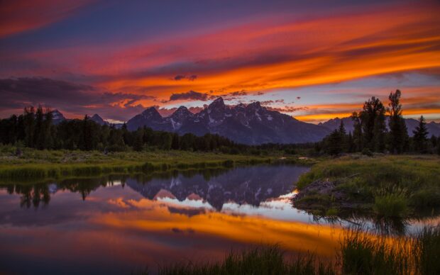 Wyoming mountain range reflects on calm water during vibrant sunset in Wyoming