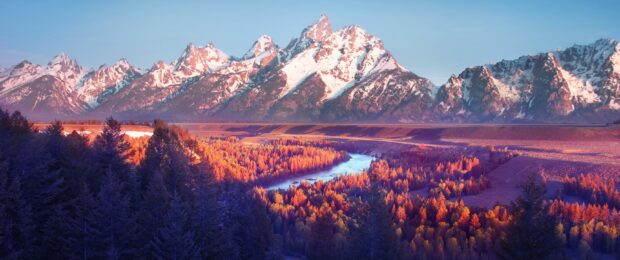 Snow covered mountain range in Wyoming with autumn forest and river in vibrant colors