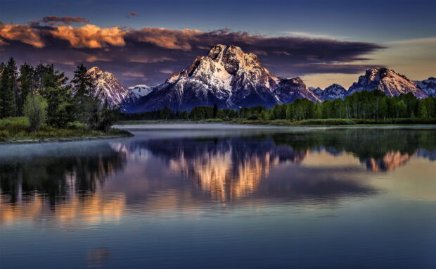 Snow covered Wyoming mountain range reflecting in calm water at sunset