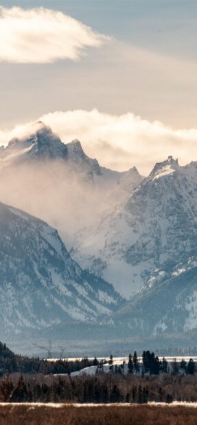 Snow covered mountain peaks in Wyoming with forest below and clouds above