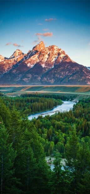 Majestic Wyoming mountain range with a river flowing through dense forest at sunrise