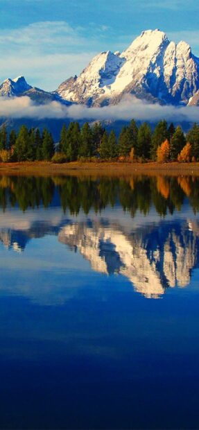 Snowy mountain range with trees reflected in calm lake in Wyoming