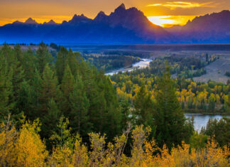 Autumn trees and river flowing through Wyoming landscape at sunset with mountain range in background