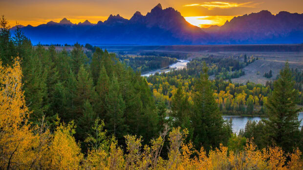 Autumn trees and river flowing through Wyoming landscape at sunset with mountain range in background