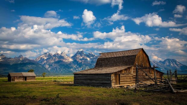 Rustic Wyoming landscape with wooden barns and mountain range under a bright blue sky