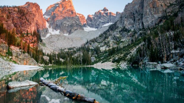 Sunrise over Wyoming mountains reflecting in a clear alpine lake with trees and rocks