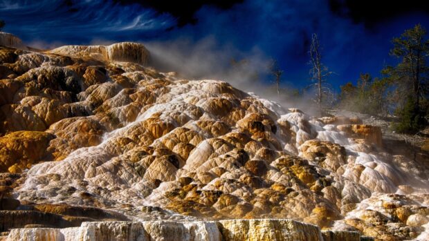 Steam rising above colorful mineral terraces in Wyoming natural landscape