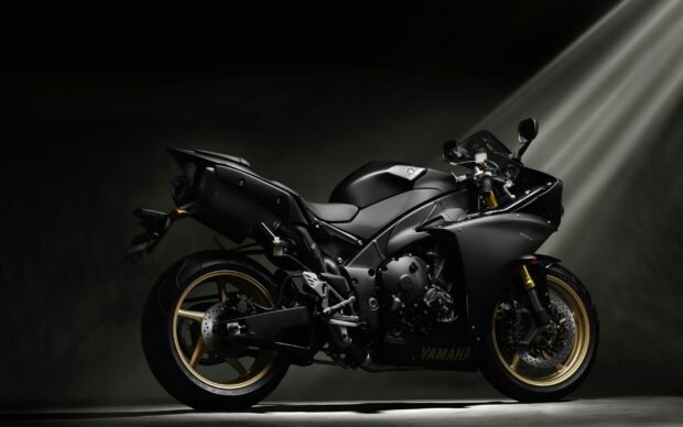 A sleek black Yamaha motorcycle with gold wheels showcased under dramatic lighting