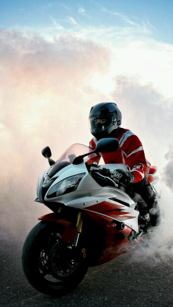 A rider in red gear riding a Yamaha motorcycle through smoky terrain at sunset