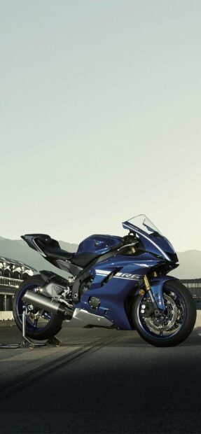 A blue Yamaha sports motorcycle parked on a racetrack with mountains in the background