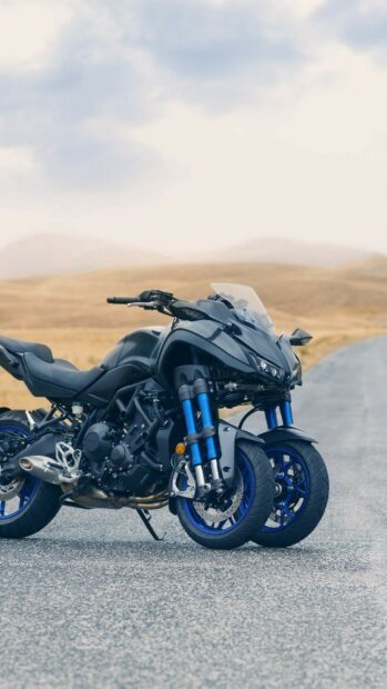 A Yamaha motorcycle with dual front wheels parked on a deserted road with dry hills in the background