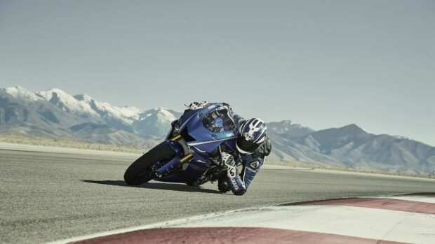 A Yamaha motorcycle leaning sharply on a race track with mountain backdrop