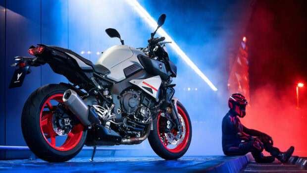 A Yamaha motorcycle parked near a rider sitting on the curb in a colorful urban night setting