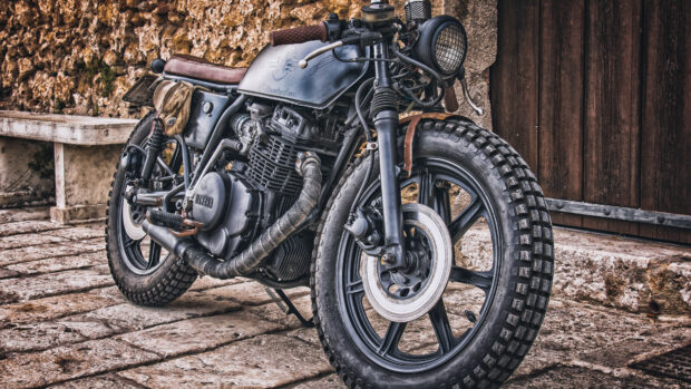 Vintage Yamaha motorcycle with rugged tires parked on stone pavement near rustic wall