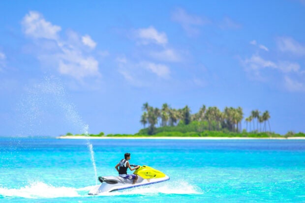 A man rides a yellow jet ski on turquoise ocean water near a tropical island, 2K Desktop Wallpaper