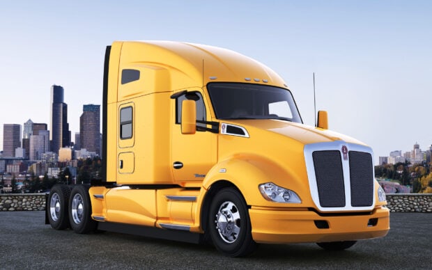 A yellow Kenworth truck is parked on a rooftop with a city skyline in the background, 2K Desktop Wallpaper
