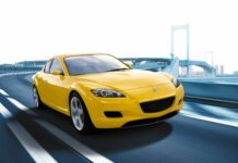 A yellow Mazda sports car is driving on a curved city bridge with a clear sky, HD Desktop Wallpaper