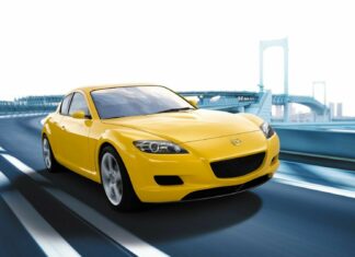 A yellow Mazda sports car is driving on a curved city bridge with a clear sky, HD Desktop Wallpaper
