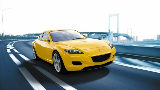 A yellow Mazda sports car is driving on a curved city bridge with a clear sky, HD Desktop Wallpaper