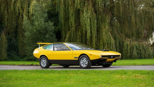 A yellow Lancia classic car parked on a green grass field with trees in the background, 2K Desktop Wallpaper