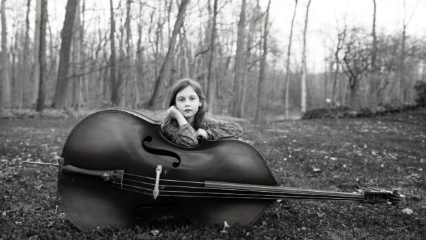 A young girl is resting her arms on a large double bass outdoors in a forest setting, 4K Desktop Wallpaper