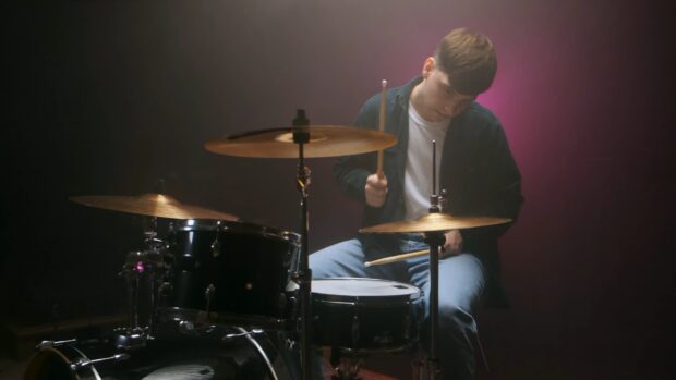 A young musician is focused on playing drums on stage with dramatic lighting, 4K Desktop Wallpaper