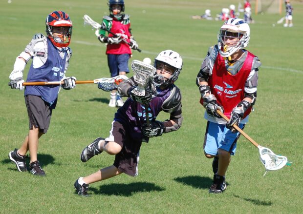 Children playing lacrosse with protective gear on grass field, HD Desktop Wallpaper