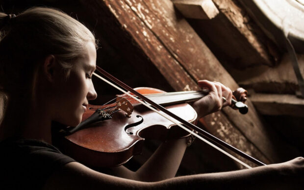 A young woman is skillfully playing a violin in a softly lit rustic room, HD Desktop Wallpaper