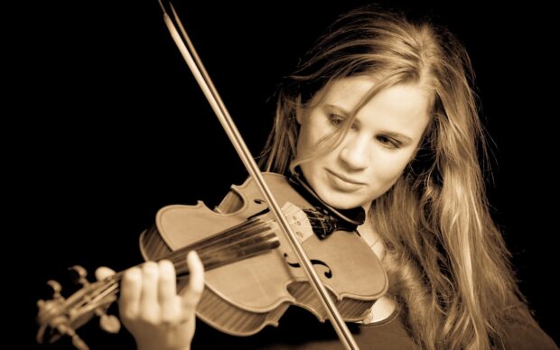 A young woman is carefully playing a classic violin with focused expression, 2K Desktop Wallpaper