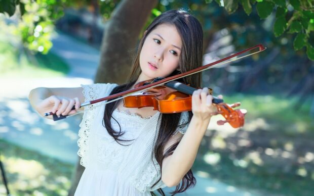 A young woman is focused as she plays the violin outdoors surrounded by greenery, 2K Desktop Wallpaper