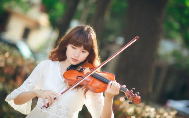 A young woman is focused on playing the violin in a natural setting, 2K Desktop Wallpaper