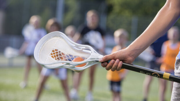 A close up of a youth holding a lacrosse stick with an orange ball on the field, HD Desktop Wallpaper