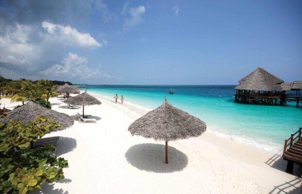 A calm Zanzibar beach shows white sand and turquoise water with huts, HD Desktop Wallpaper