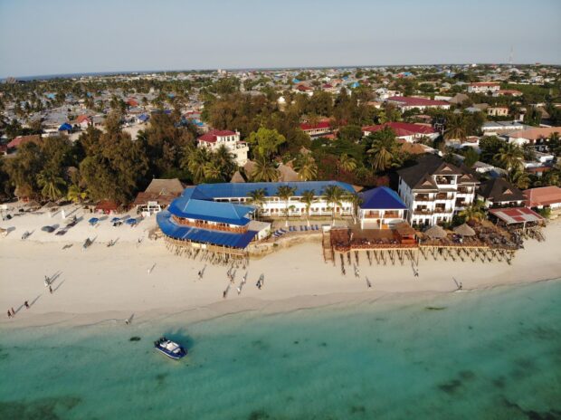 An aerial view of Zanzibar reveals a coastal town with buildings and a beach by the clear sea, HD Desktop Wallpaper