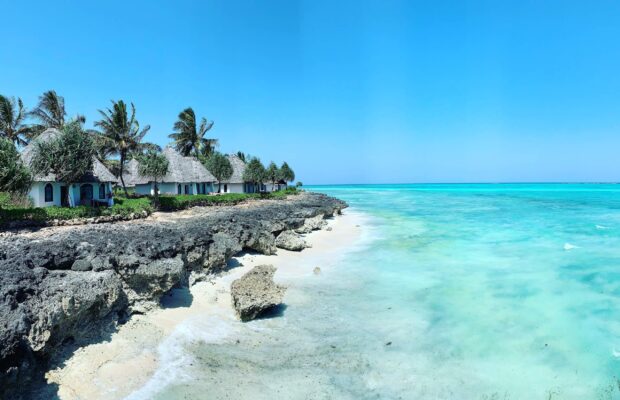 A serene view of Zanzibar with clear turquoise waters and rocky shores under a bright blue sky, 2K Desktop Wallpaper