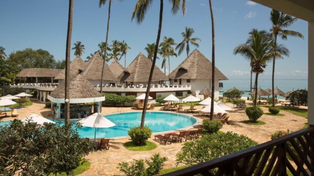 A tropical resort in Zanzibar features palm trees and thatched roofs near a swimming pool, HD Desktop Wallpaper