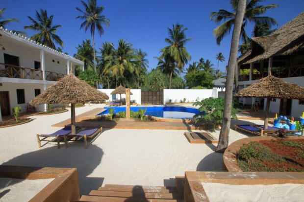 A tropical resort in Zanzibar features palm trees and sun loungers near a pool, 2K Desktop Wallpaper