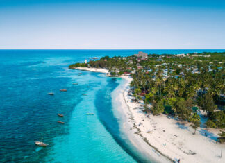 The turquoise ocean meets the white sandy shore at Zanzibar with boats floating near the coast, HD Desktop Wallpaper
