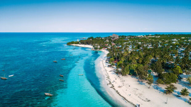 The turquoise ocean meets the white sandy shore at Zanzibar with boats floating near the coast, HD Desktop Wallpaper