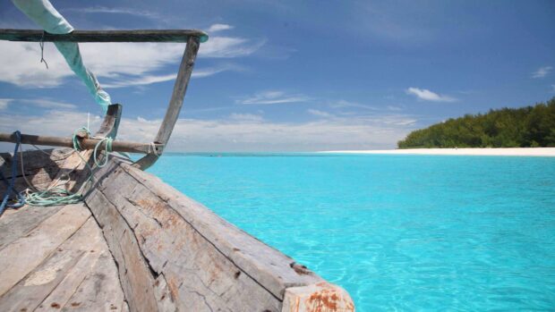 A wooden boat floats on clear turquoise water in Zanzibar, HD Desktop Wallpaper