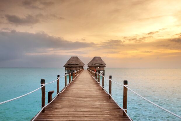 A wooden pier in Zanzibar stretches into calm turquoise waters under a golden sky, 2K Desktop Wallpaper