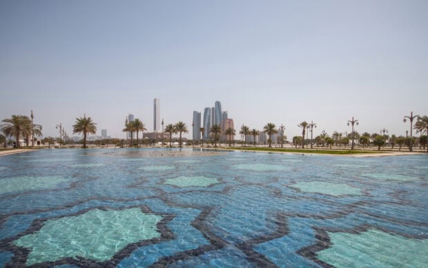 Clear blue decorative pool with palm trees and Abu Dhabi skyline in the distance