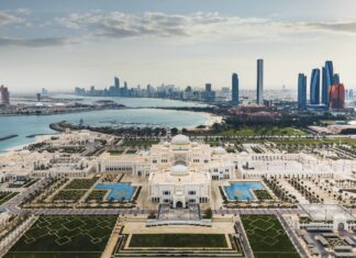 Aerial view of Abu Dhabi cityscape featuring a grand palace and modern skyscrapers under cloudy sky