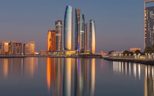 Modern Abu Dhabi skyline with illuminated skyscrapers reflecting on calm water at dusk
