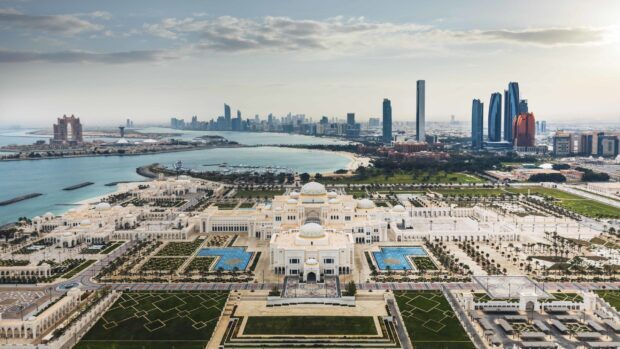 Aerial view of Abu Dhabi cityscape featuring a grand palace and modern skyscrapers under cloudy sky