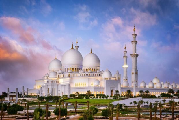 The Sheikh Zayed Mosque in Abu Dhabi showcases stunning white domes and minarets under a colorful evening sky